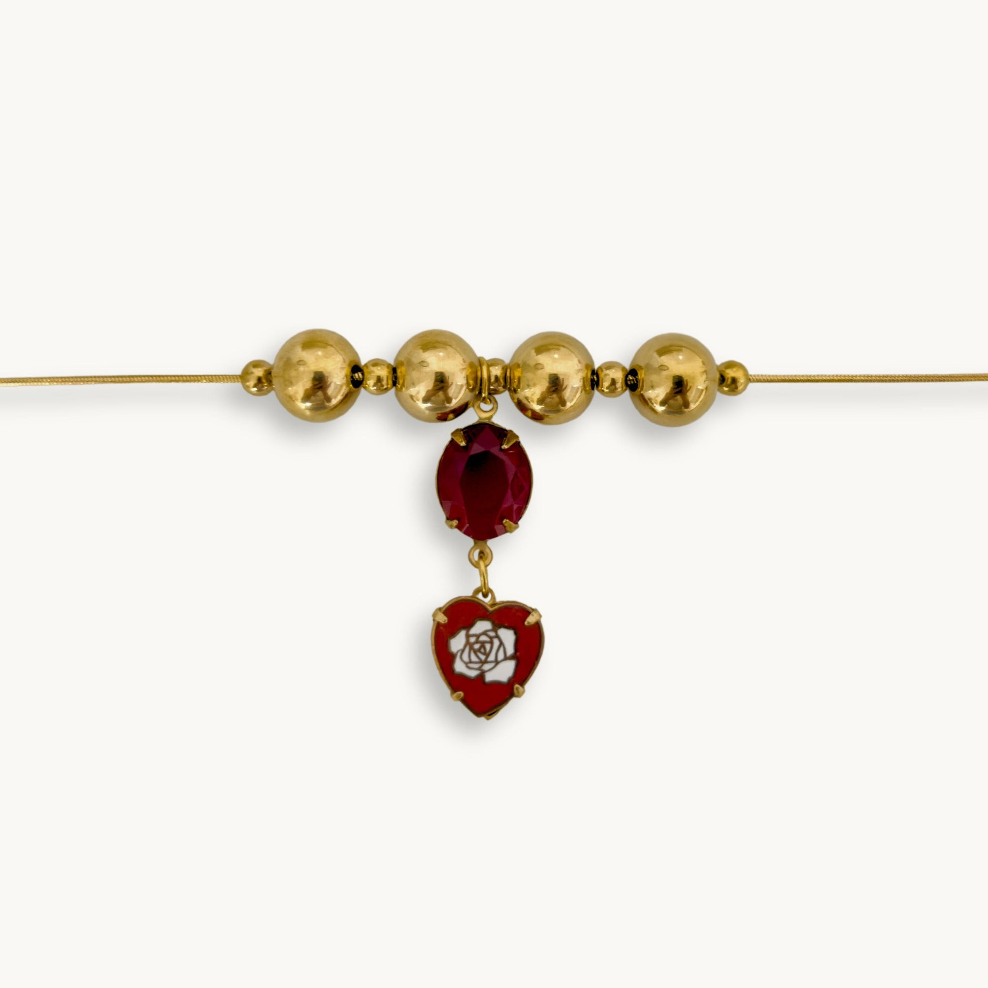 Close-up of the Inez Necklace featuring a gold snake chain, red oval stone, and vintage heart drop.