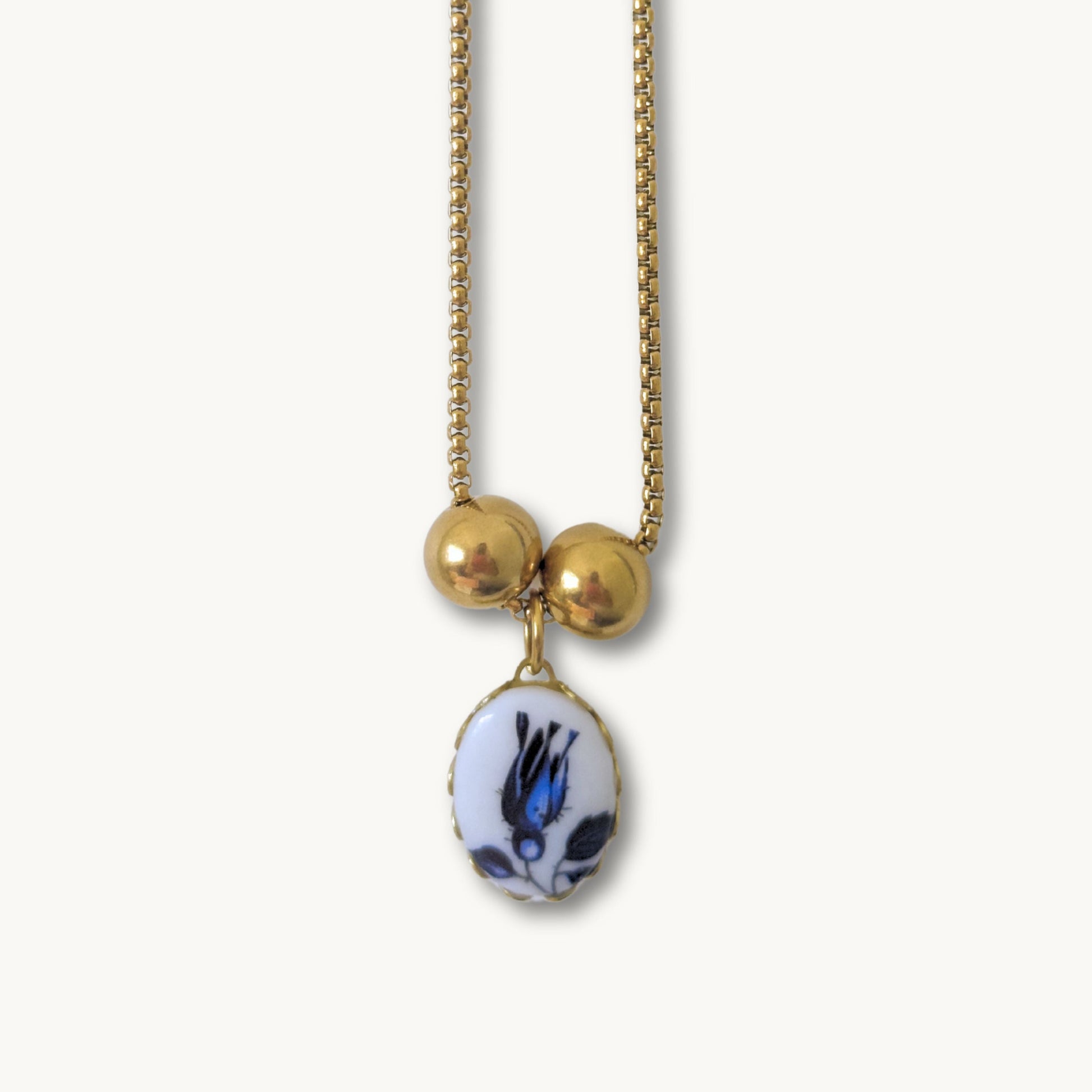 Close-up of the Phylis Necklace showcasing its delicate blue tulip ceramic pendant on a gold-plated cross chain.