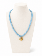 A light blue beaded necklace with a gold tiger head pendant, displayed on a cream-colored jewelry bust against a white background.