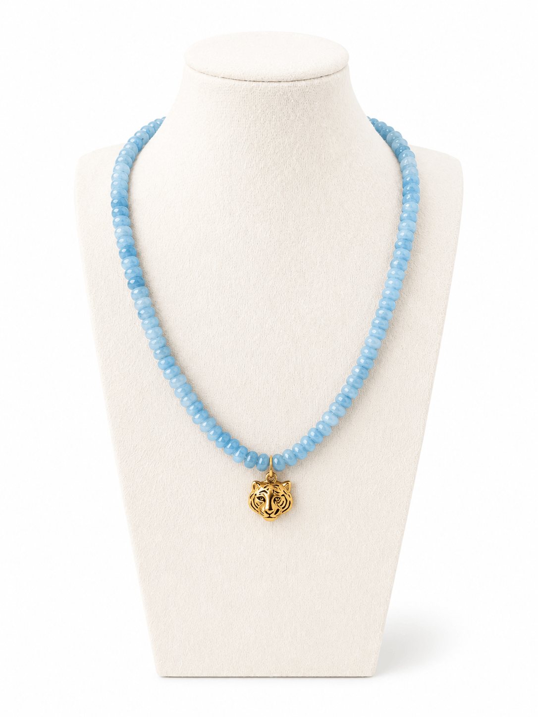 A light blue beaded necklace with a gold tiger head pendant, displayed on a cream-colored jewelry bust against a white background.