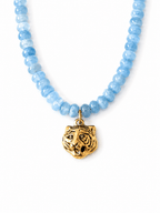 A beaded necklace featuring light blue faceted gemstone beads and a textured gold tiger head pendant, displayed on a clean white background.