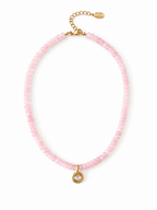 A delicate pink beaded necklace with a small gold pendant featuring a clear faceted gemstone, displayed on a clean white background.