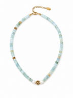 A beaded necklace featuring light blue, green, and beige stone beads with a gold-tone flower charm and extender chain, displayed on a clean white background.