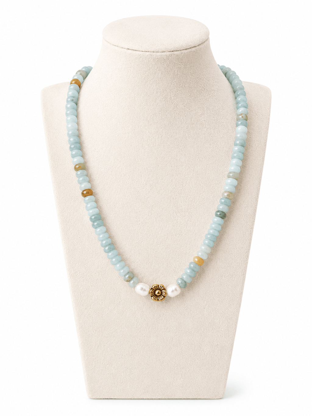 A beaded necklace displayed on a cream jewelry bust. The necklace features light blue stone beads, small white beads, a few tan/gold beads, and a central gold-toned floral or sunburst charm with clear stones.
