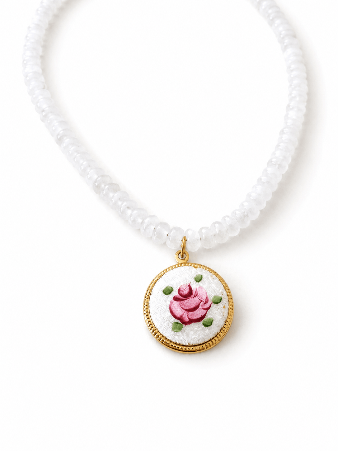 A white beaded necklace featuring a round pendant with a gold-tone border and a white enamel background decorated with a pink rose and green leaves.