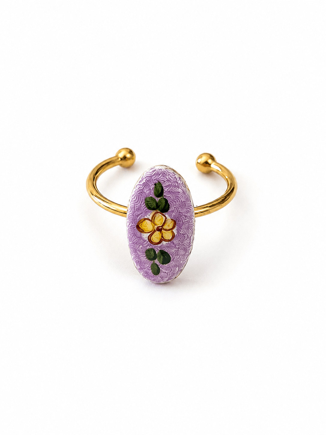 A gold-plated open cuff ring featuring a textured lavender purple oval centerpiece decorated with a yellow flower and green leaves, set against a plain white background.