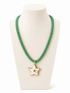 A green beaded necklace with a white enamel star pendant outlined in gold, displayed on a cream-colored jewelry bust against a white background.