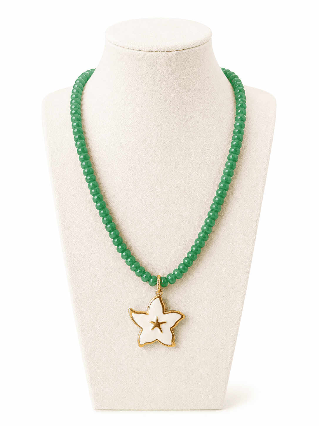 A green beaded necklace with a white enamel star pendant outlined in gold, displayed on a cream-colored jewelry bust against a white background.