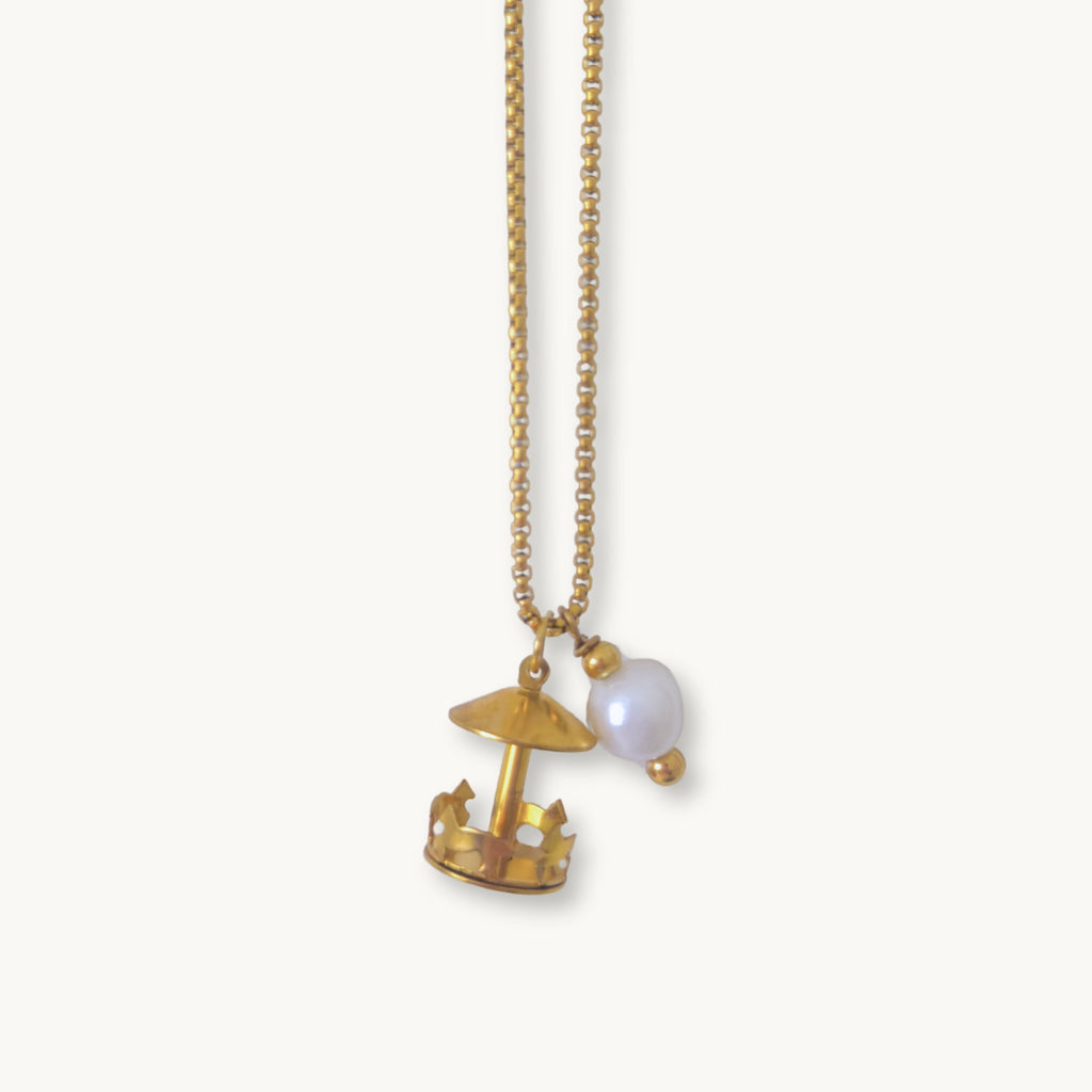 Close-up of the Gertrude Necklace featuring a detailed spinning merry-go-round charm and freshwater pearl accent on a gold-plated chain.