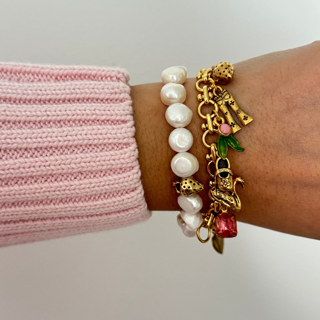 Close-up of gold-plated bracelet with pink stone heart locket and glass pearl charm