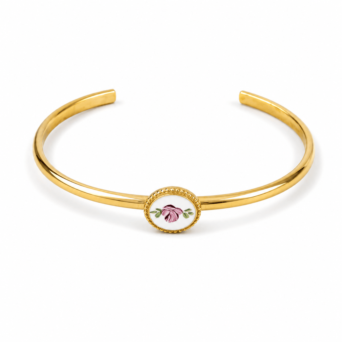A polished gold-tone open cuff bracelet featuring a central oval bezel-set floral charm with pink and green enamel details, shown on a clean white background.