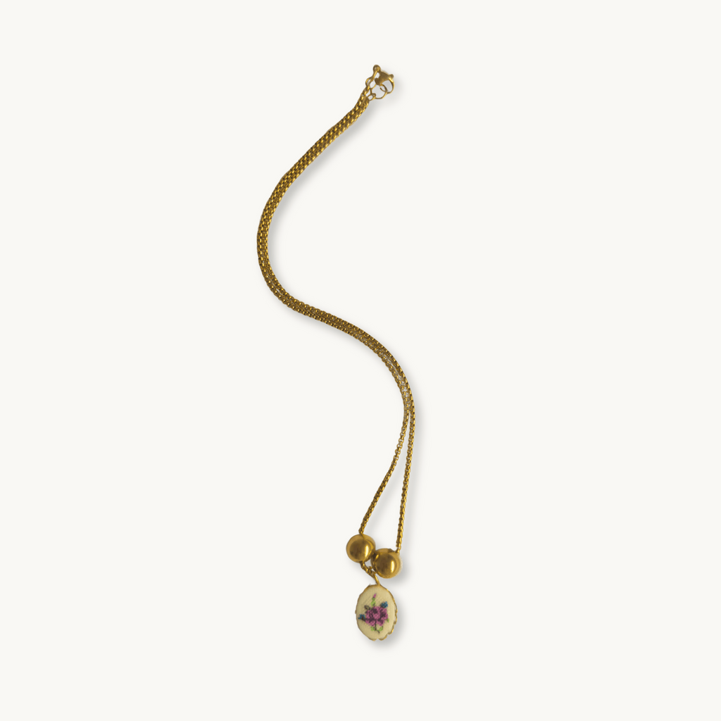 Hilda Necklace - 18K gold-plated cross chain with a delicate purple flower needlework pendant set on brass or gold plating, accented by gold-plated spacer beads, 17 inches in length.
