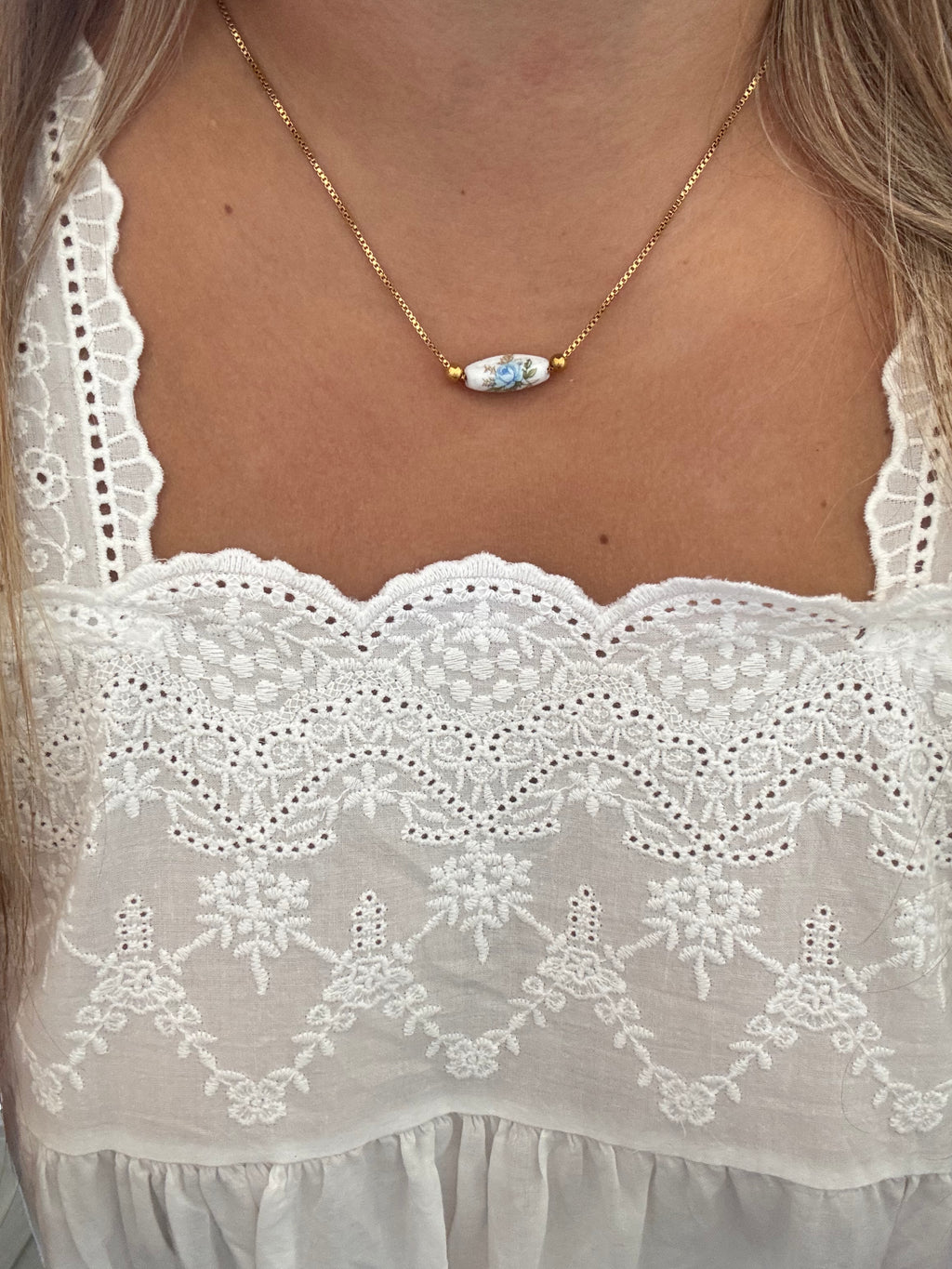Model wearing The Lilibeth Necklace featuring a vintage blue rose ceramic Limoge tube on a box chain with a needle lock. Adjustable length of 17 inches for comfort and style.