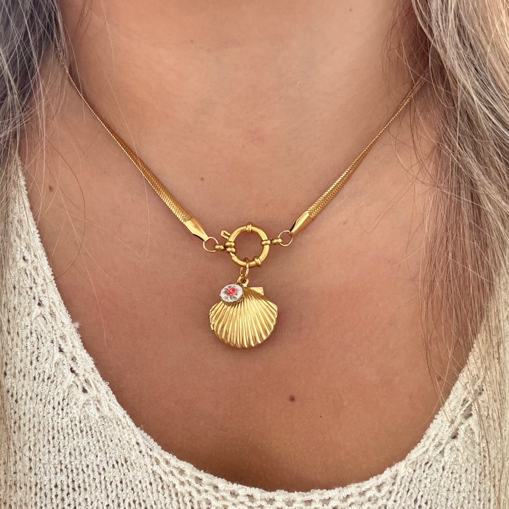 Model wearing the CiCi Necklace, featuring a chunky 18K gold-plated snake chain, sailor clasp, gold shell locket, and a tiny round flower ceramic set on brass.