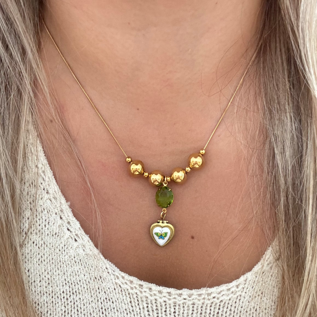 Model wearing The Miel Necklace featuring an 18K PVD gold plated snake chain with spacer beads, a lime green oval stone drop, and a vintage brass locket. 17 inches in length.