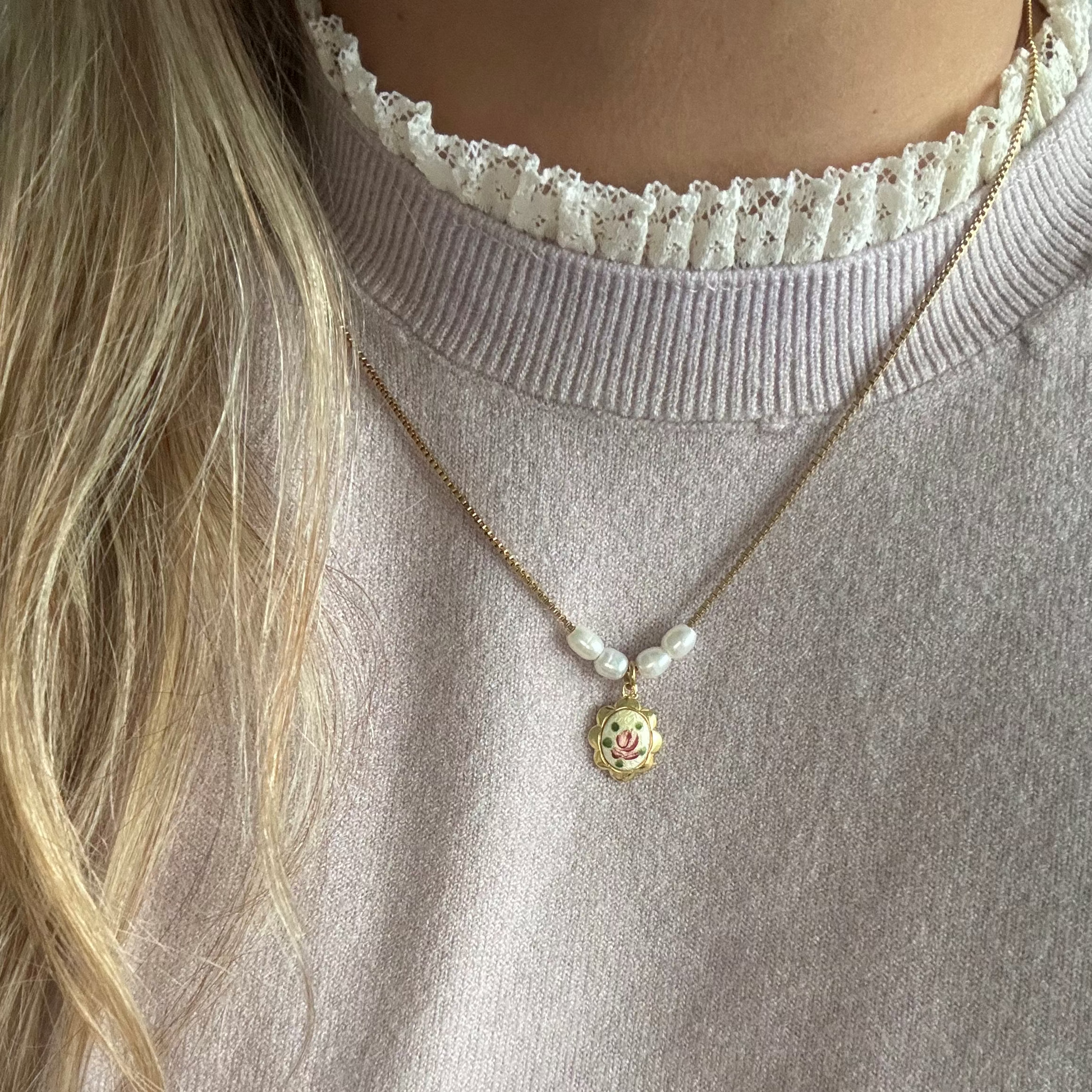 Model wearing the Betina Necklace — a dainty gold chain adorned with handpicked vintage charms and a soft pink accent, styled for a timeless and elegant everyday look.