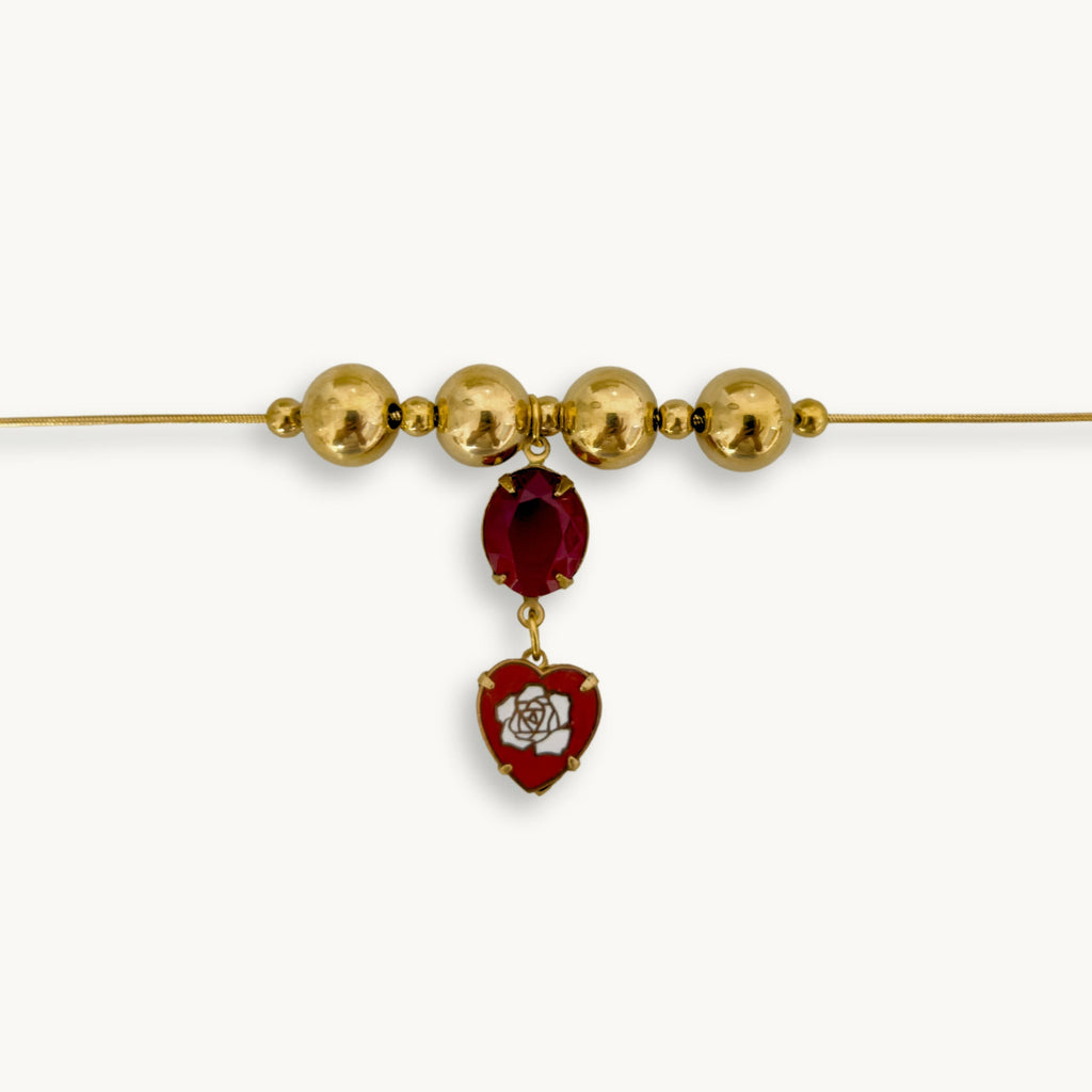 Close-up of the Inez Necklace featuring a gold snake chain, red oval stone, and vintage heart drop.