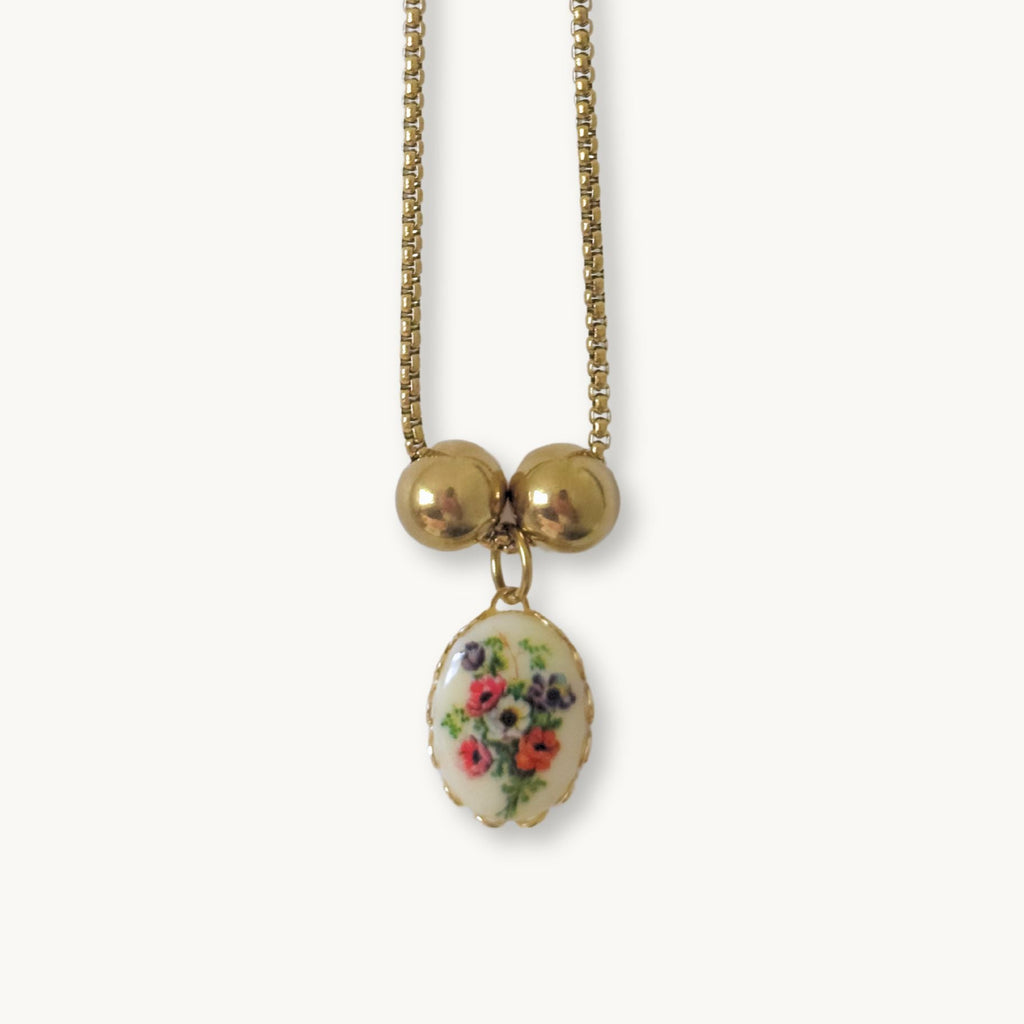 Close-up of the Lily Necklace showcasing its poppy bouquet ceramic pendant and gold-plated frame.