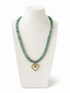 A beaded necklace in a translucent light green tone with a small gold heart-shaped pendant, displayed on a white jewelry bust against a white background.