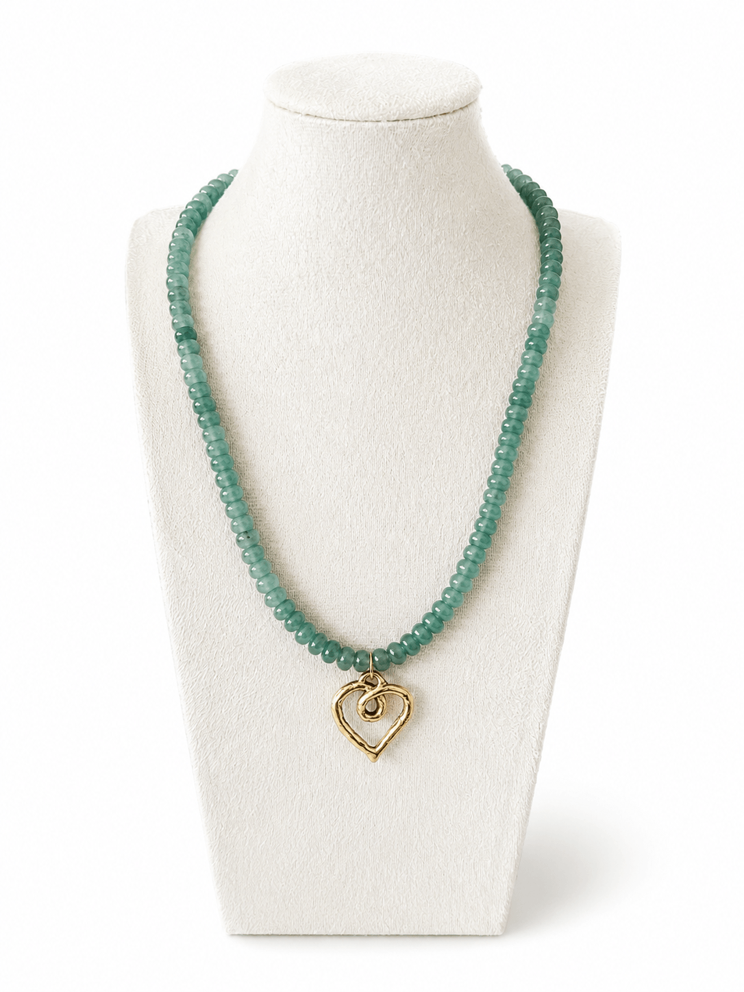 A beaded necklace in a translucent light green tone with a small gold heart-shaped pendant, displayed on a white jewelry bust against a white background.