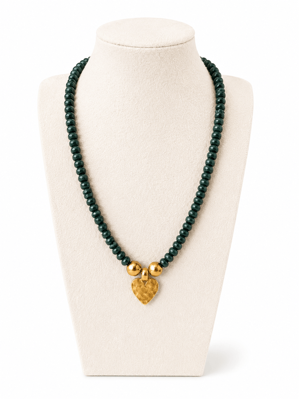 A beaded necklace displayed on a cream jewelry bust. The necklace consists of dark green round beads with two small gold spacer beads and a textured gold heart-shaped pendant.