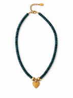 A beaded necklace featuring dark teal-green beads and a textured gold heart charm, displayed on a clean white background.