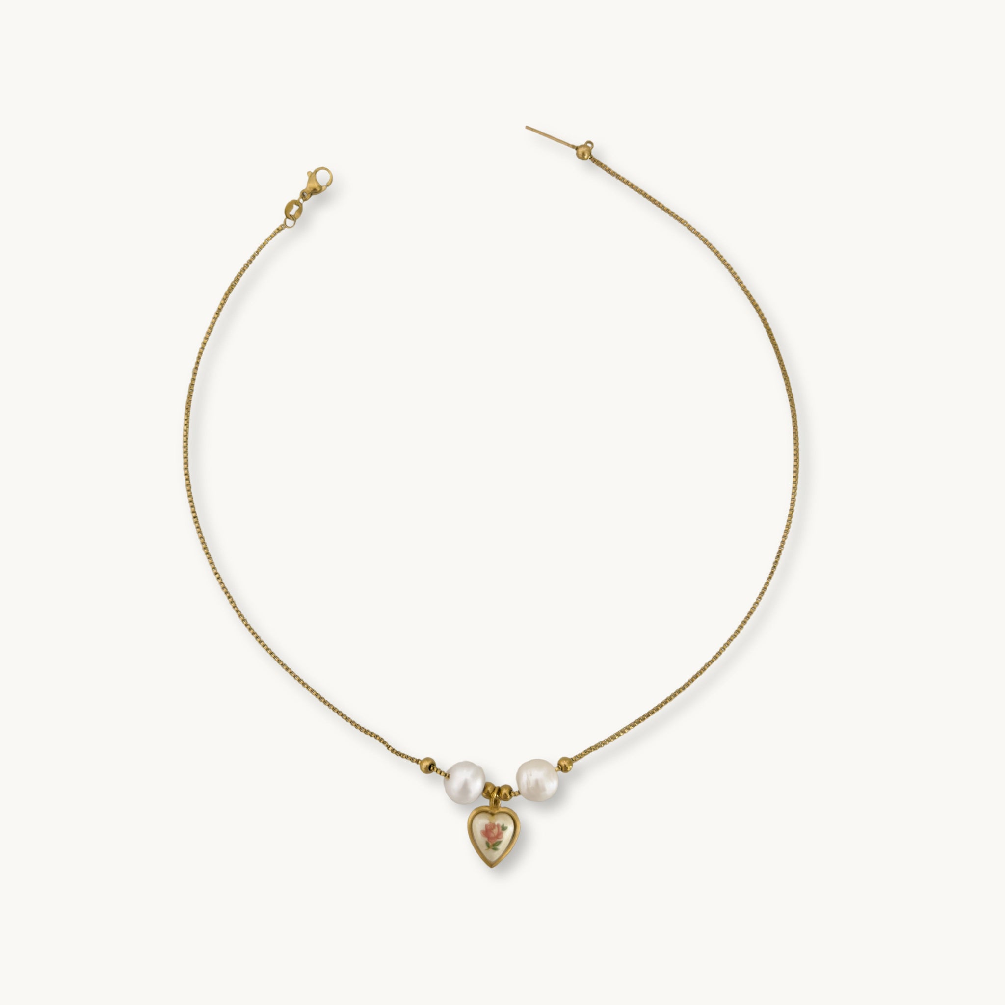 Elegant Monica Necklace displayed on a jewelry stand, showcasing its timeless design with pearls and a brass heart pendant.