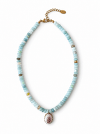 A beaded necklace featuring light blue, mint green, and white stone beads with small gold spacer beads, a gold chain extender, and a central oval pendant with a pink and white floral design.