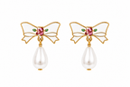 A pair of gold bow earrings with white enamel, a pink rhinestone center, small green enamel leaves, and a dangling white pearl teardrop below each bow.