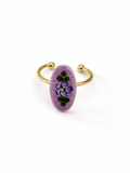 A gold-plated open cuff ring featuring a textured, oval-shaped lavender purple stone inlaid with a hand-painted purple pansy and green leaves, set against a plain white background.