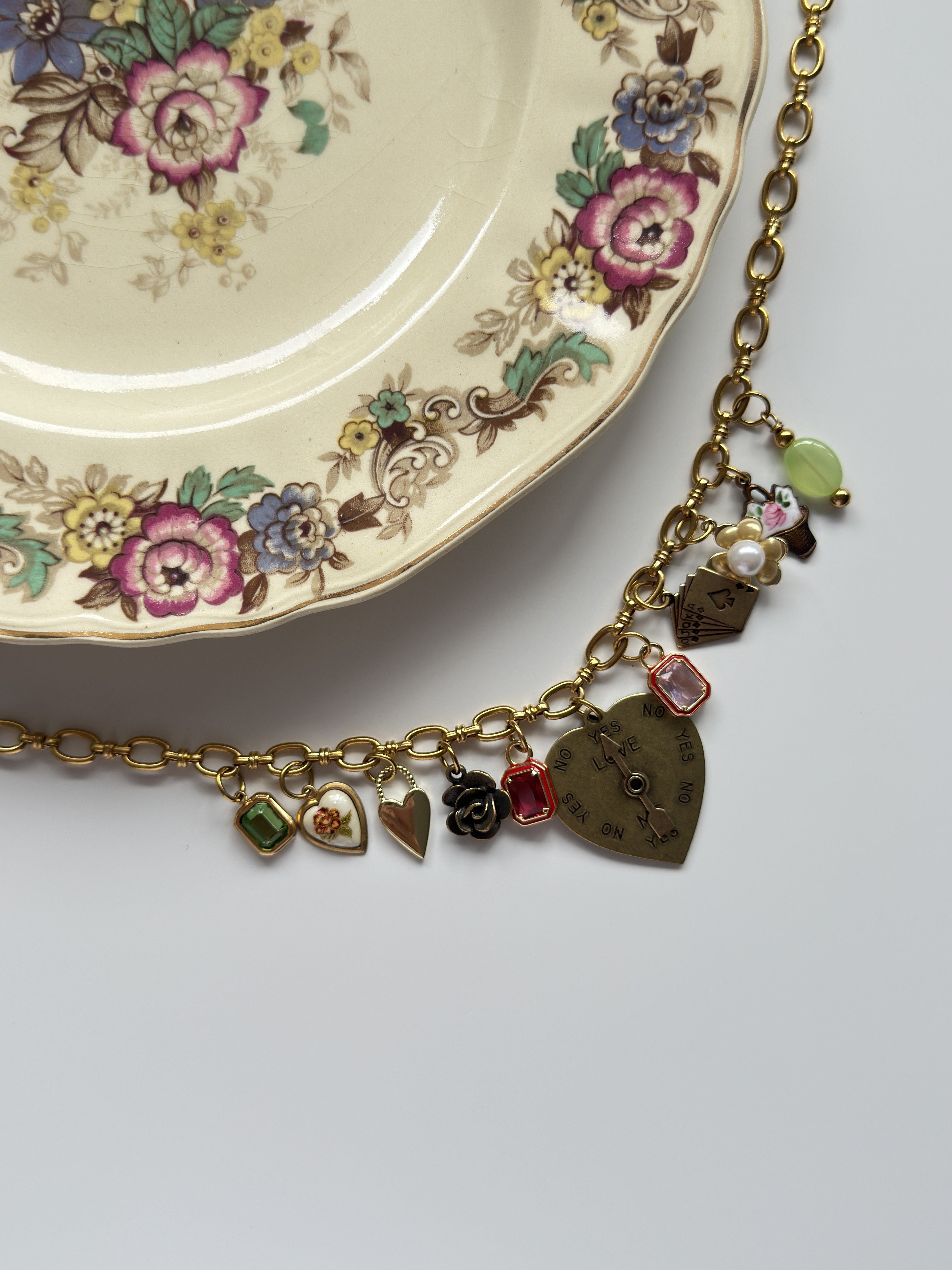 Flatlay of vintage gold charm necklace displayed on a ceramic plate – limited edition piece.